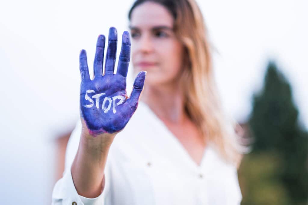 Kobieta z wyciągniętą ręką. Wnętrze dłoni ma pomalowane na fioletowo i na tym biały napis STOP
